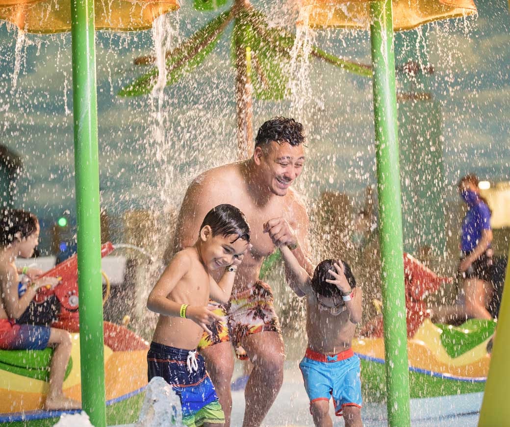 Father is playing with kids in the toddler play area of the water park