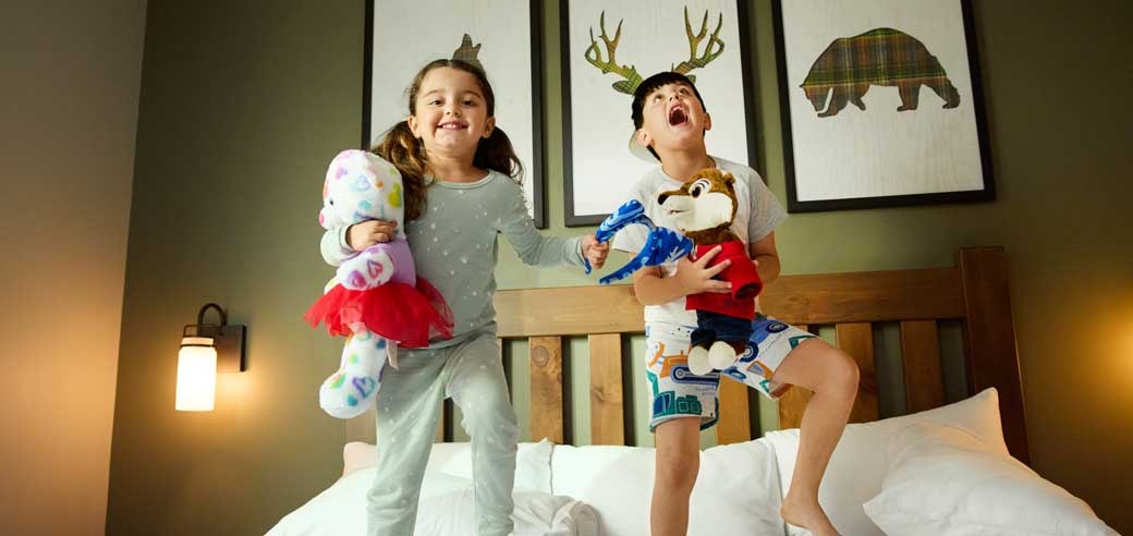 Two kids jumping on a bed in a Great Wolf Lodge Suite