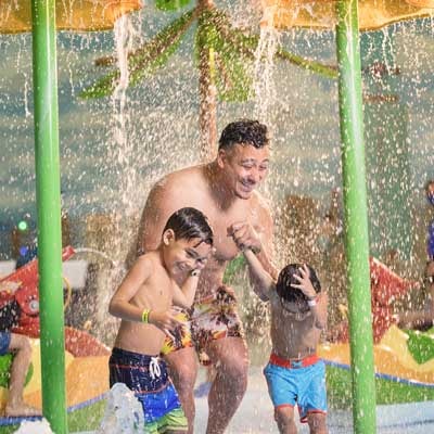 Father is playing with kids in the toddler play area of the water park